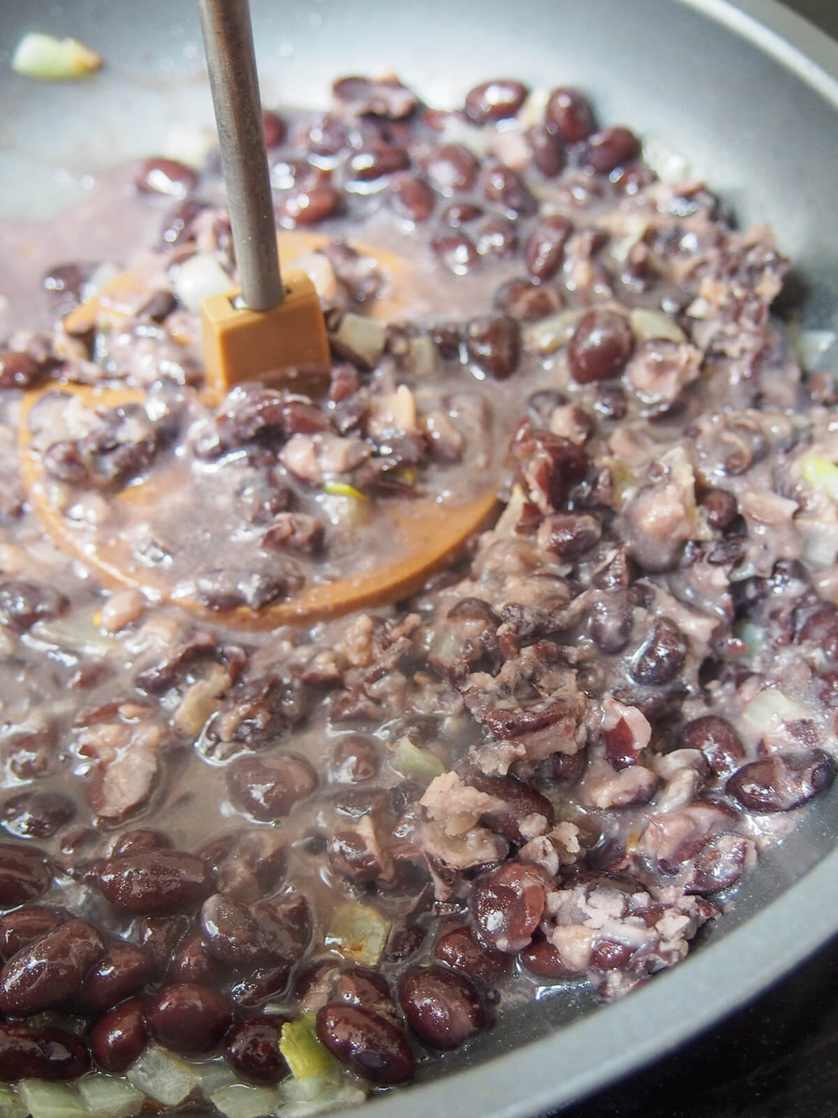 mashing black beans, onion and stock in a skillet