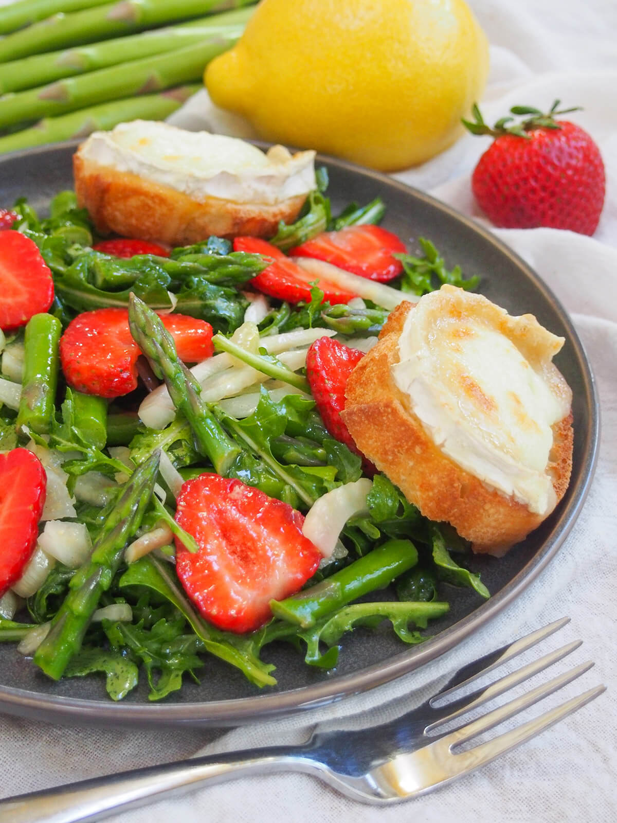 side partial view of strawberry asparagus salad with fork in front of plate