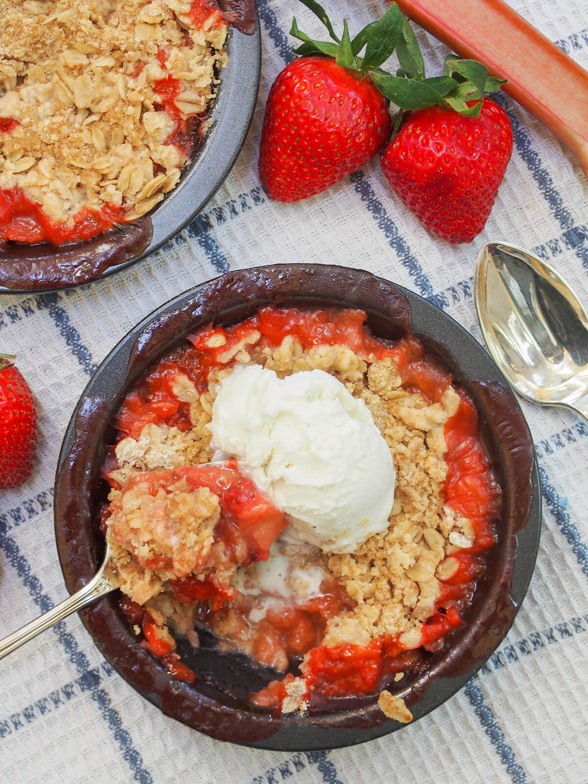 This strawberry rhubarb crisp is a delicious combination of sweet juicy strawberries, a touch of tartness from the rhubarb, and a crisp oat crumble topping. It's easy to make, comforting and the perfect treat for spring. dish of strawberry rhubarb crisp with spoon to side and ice cream on top, strawberries above dish