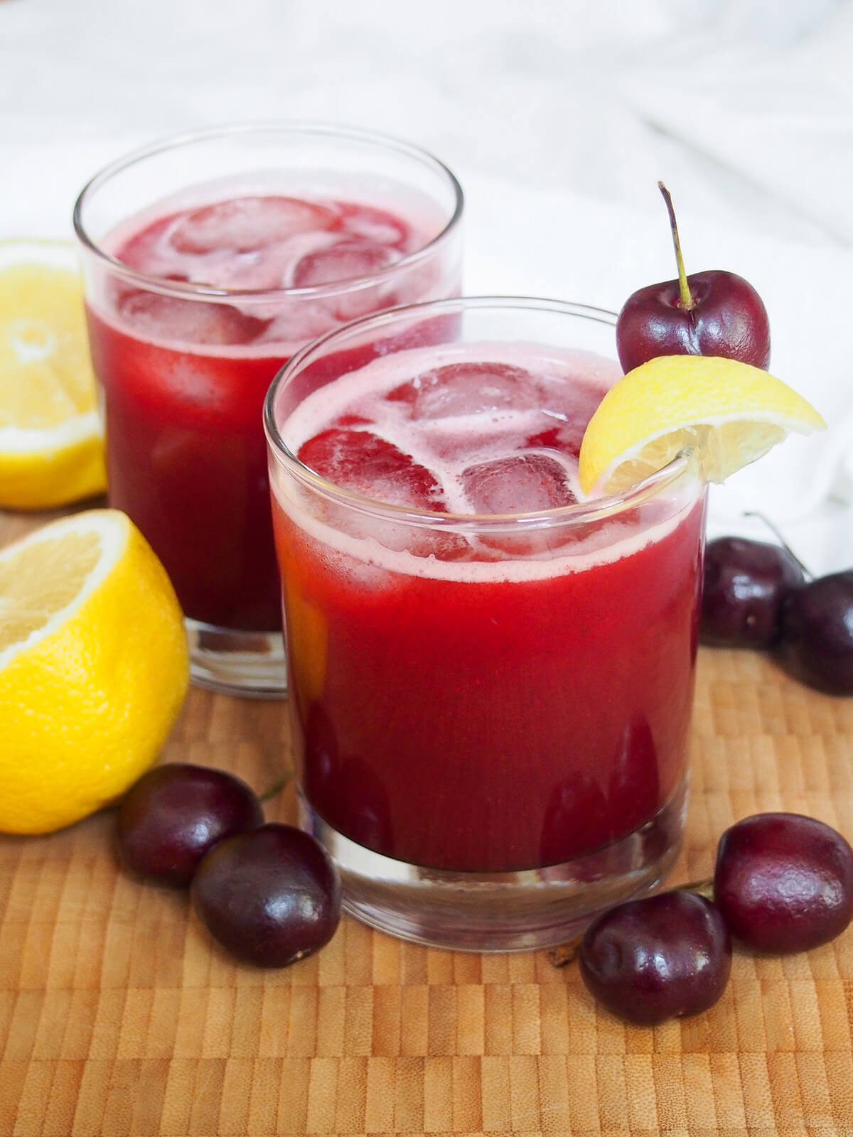 two glasses of cherry lemonade on wooden board with fruit to side