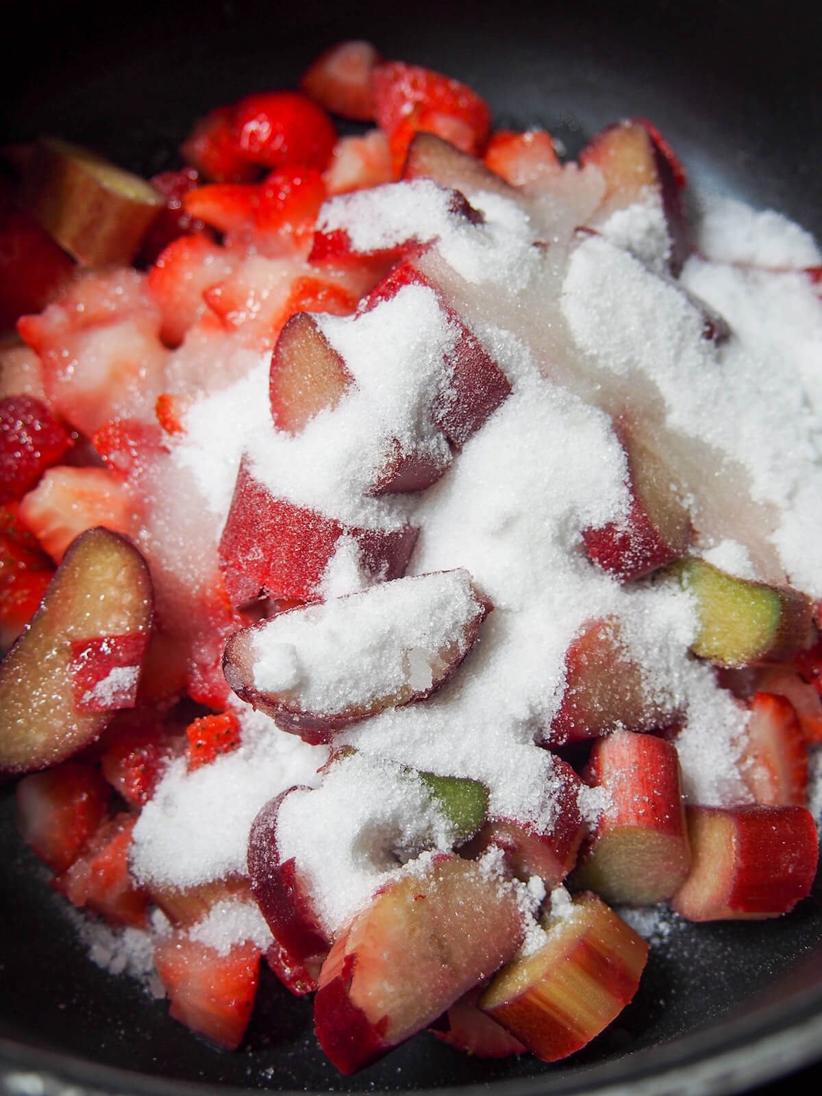 sliced strawberries and rhubarb with sugar over them in pot