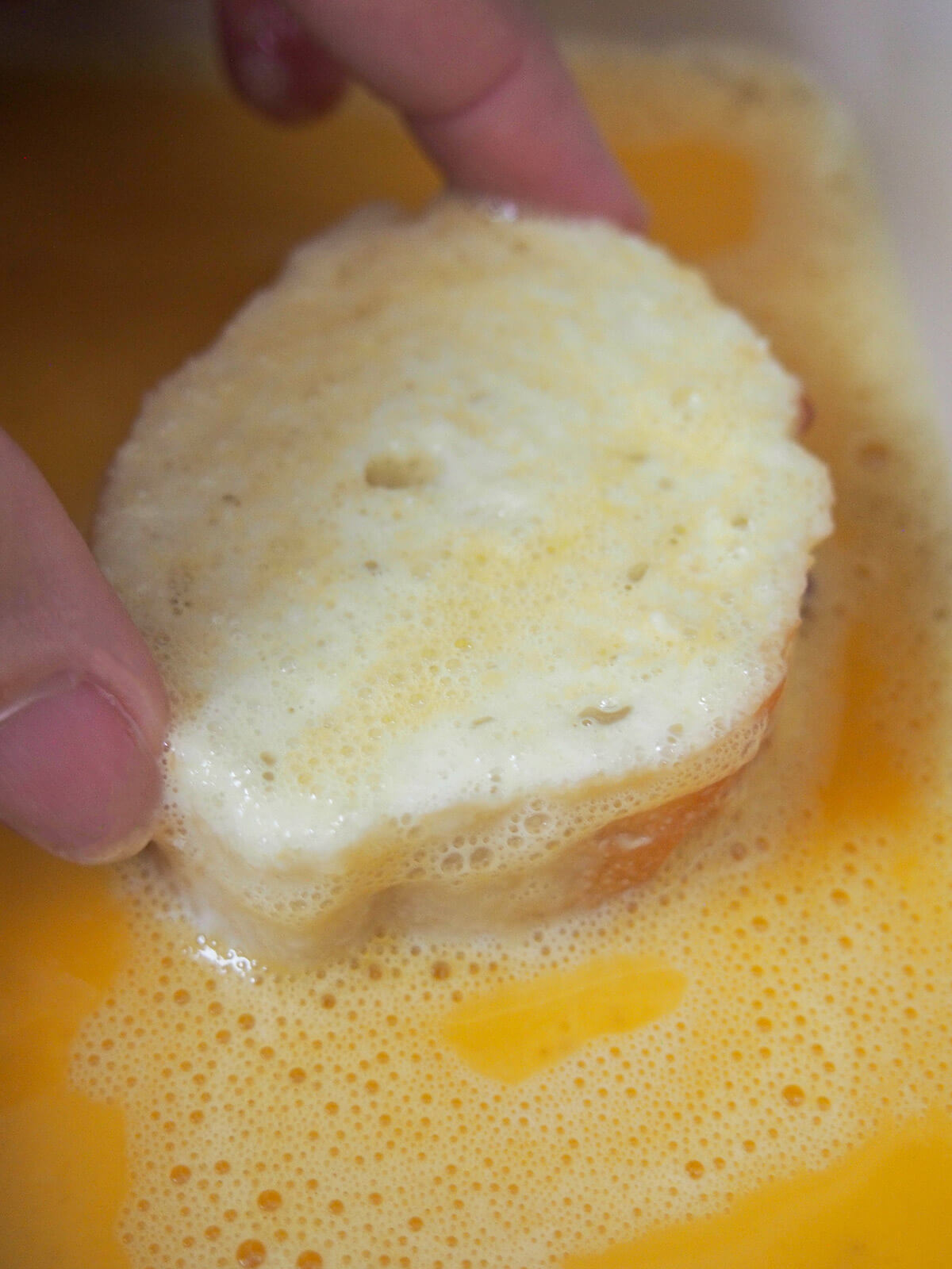 dipping a soaked piece of bread in egg