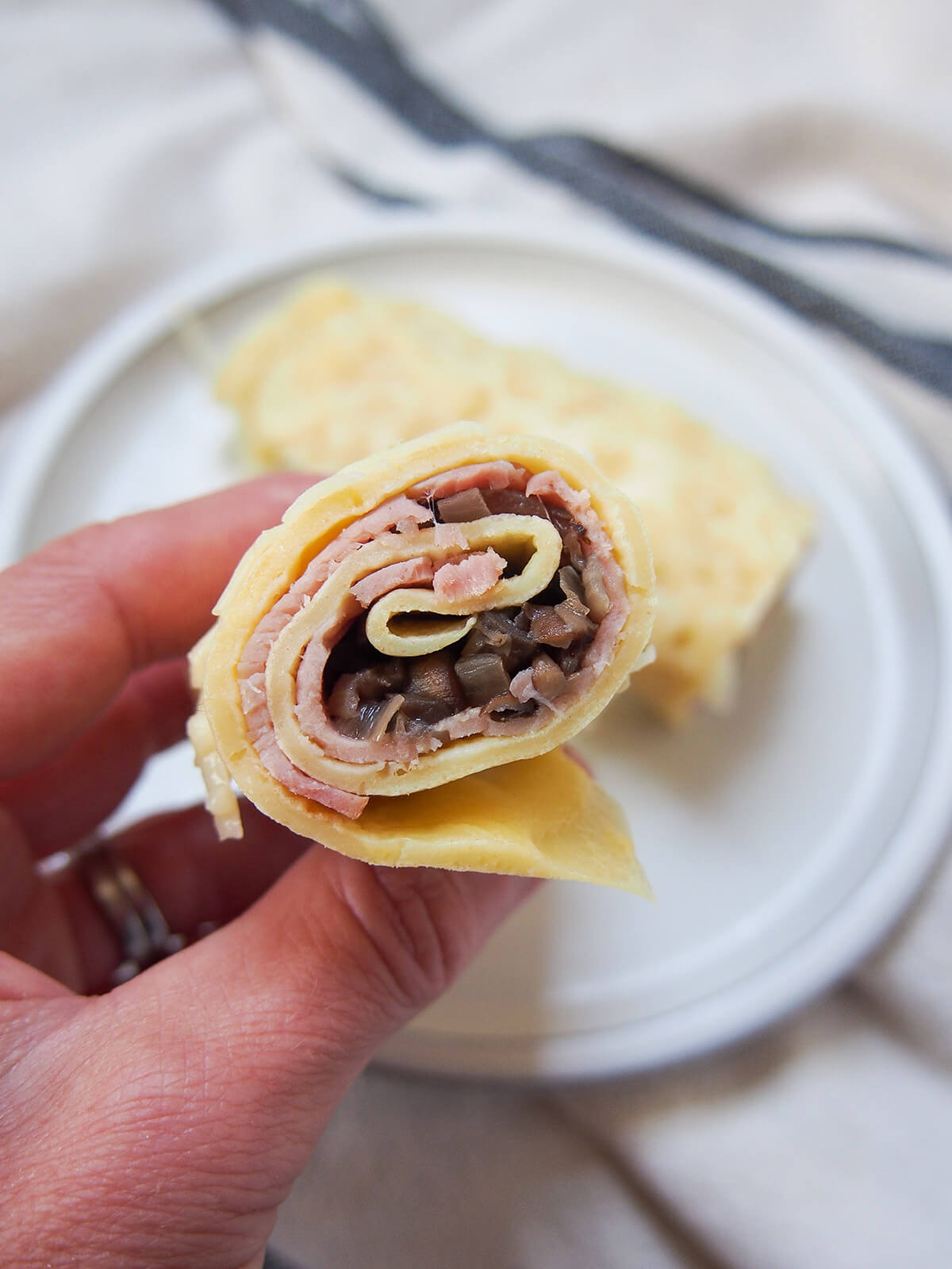 holding part of a ham crepe in hand showing rolls of ham, mushroom filling in layers of crepe