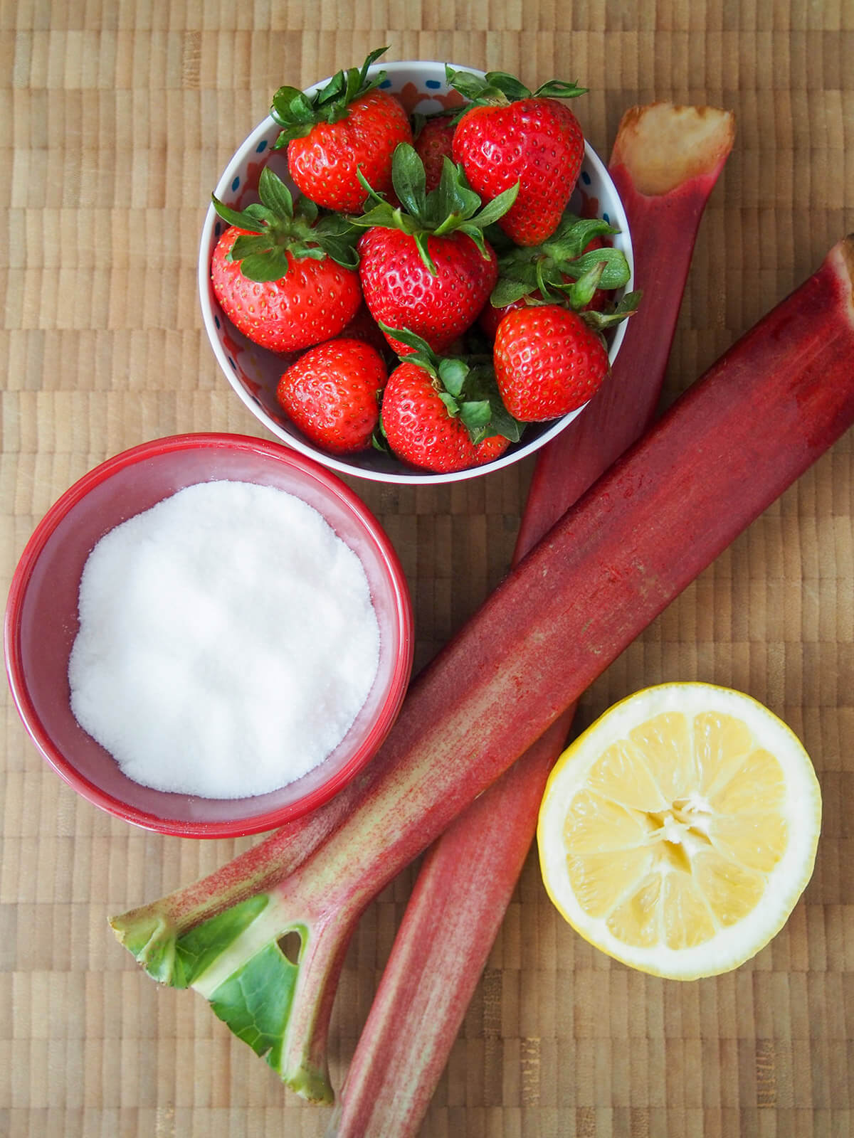 bowls of strawberries, sugar and rhubarb stems with part lemon below