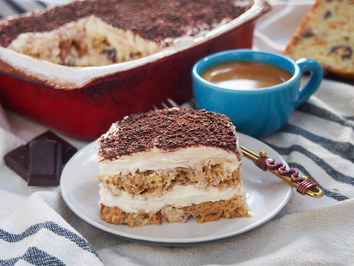 slice of panettone tiramisu in front of rest of dish and cup of espresso coffee.