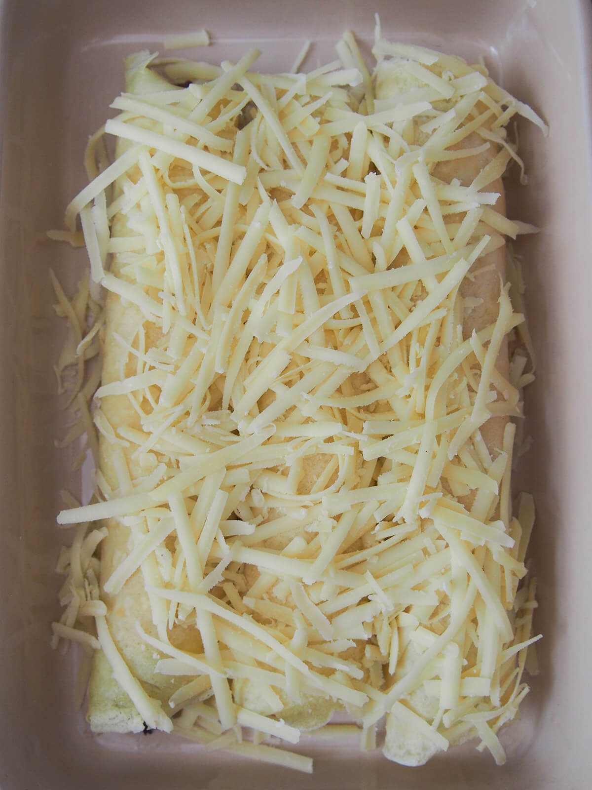 grated cheese over rolled crepes in dish