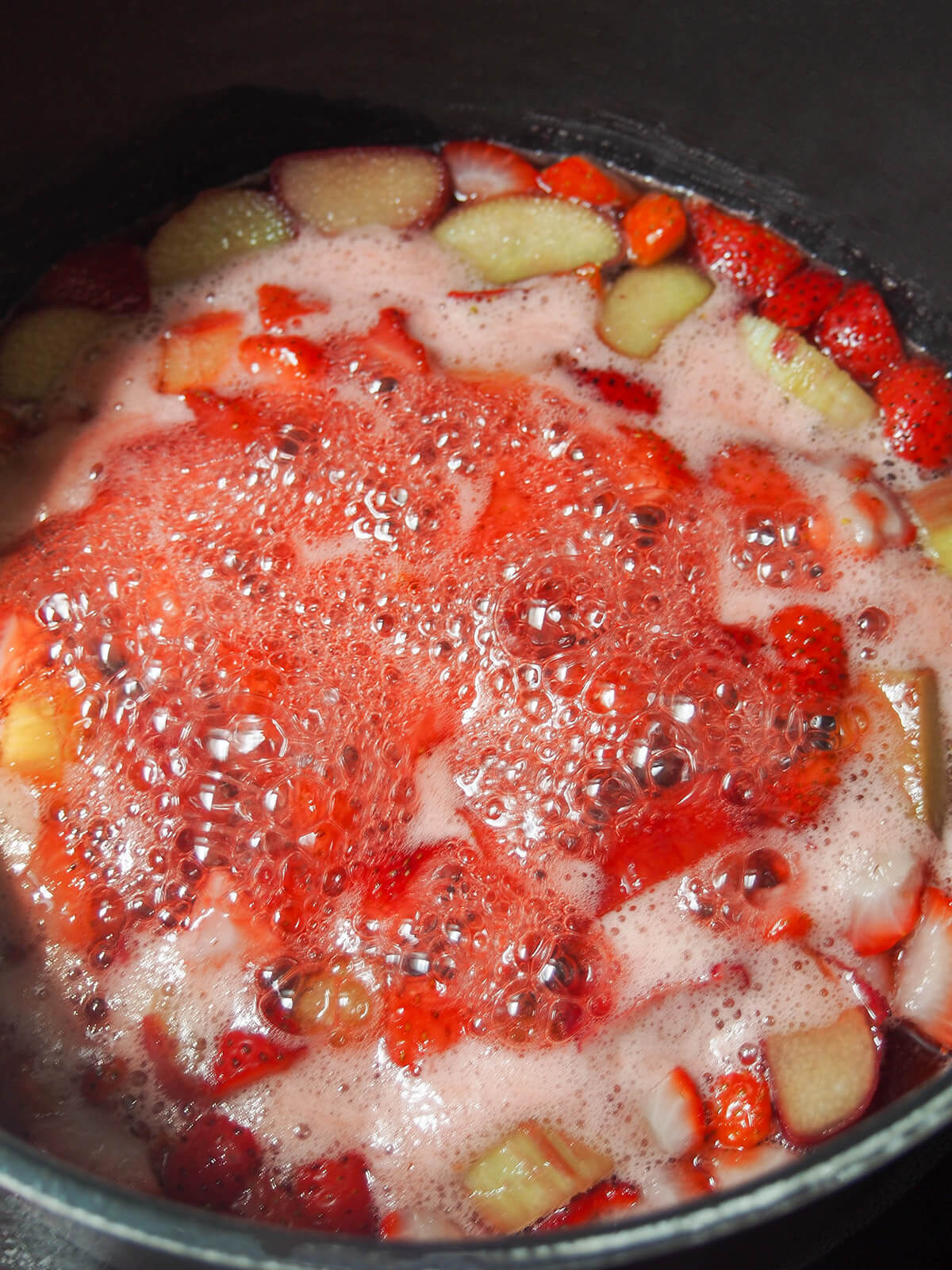 simmering liquid with chunks of rhubarb and strawberry visible around edges