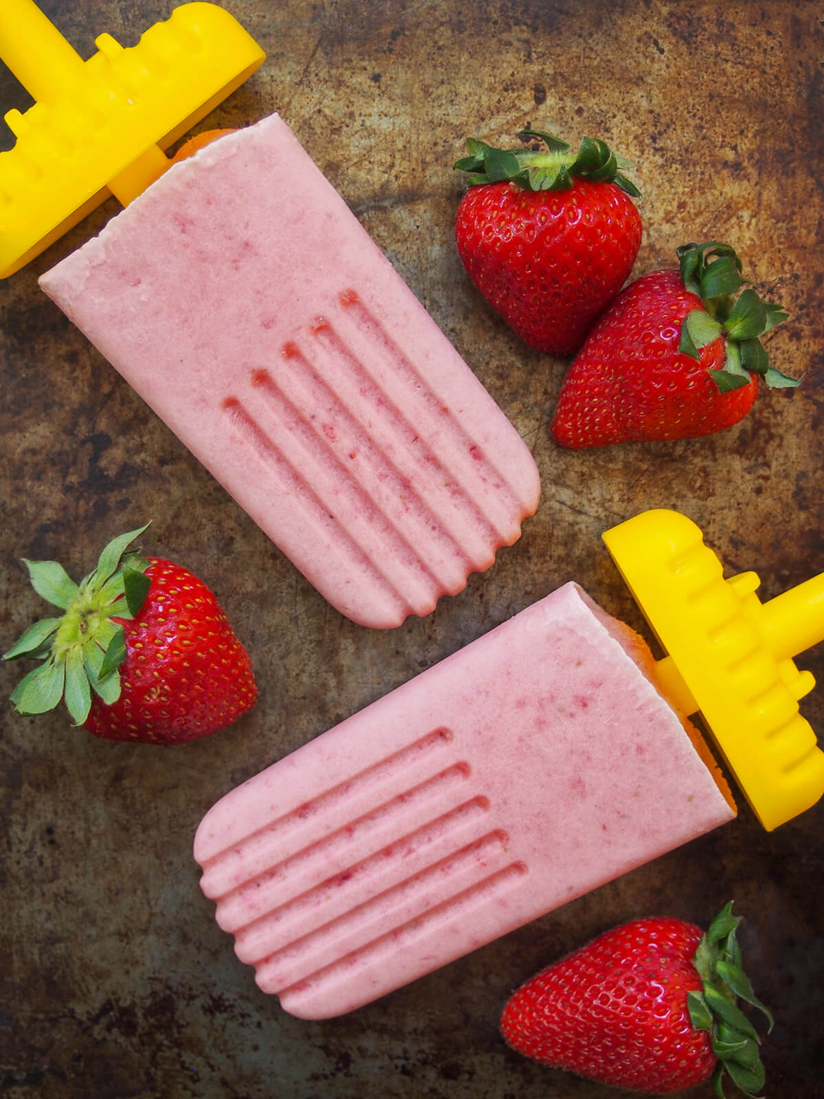 two paletas de fresa con crema (strawberry popsicles) with strawberries to either side