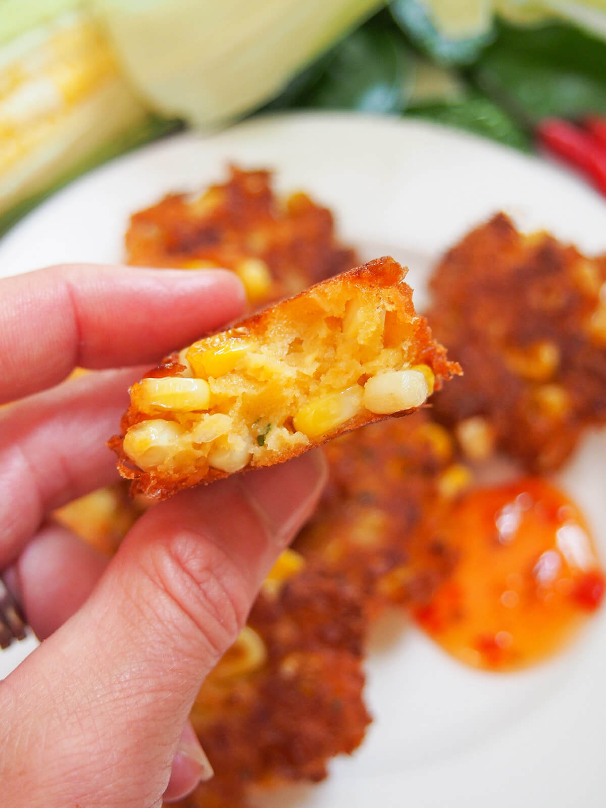 holding a Thai corn fritter in hand above plate of more