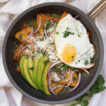 skillet of chilaquiles verdes topped with egg and avocado slices
