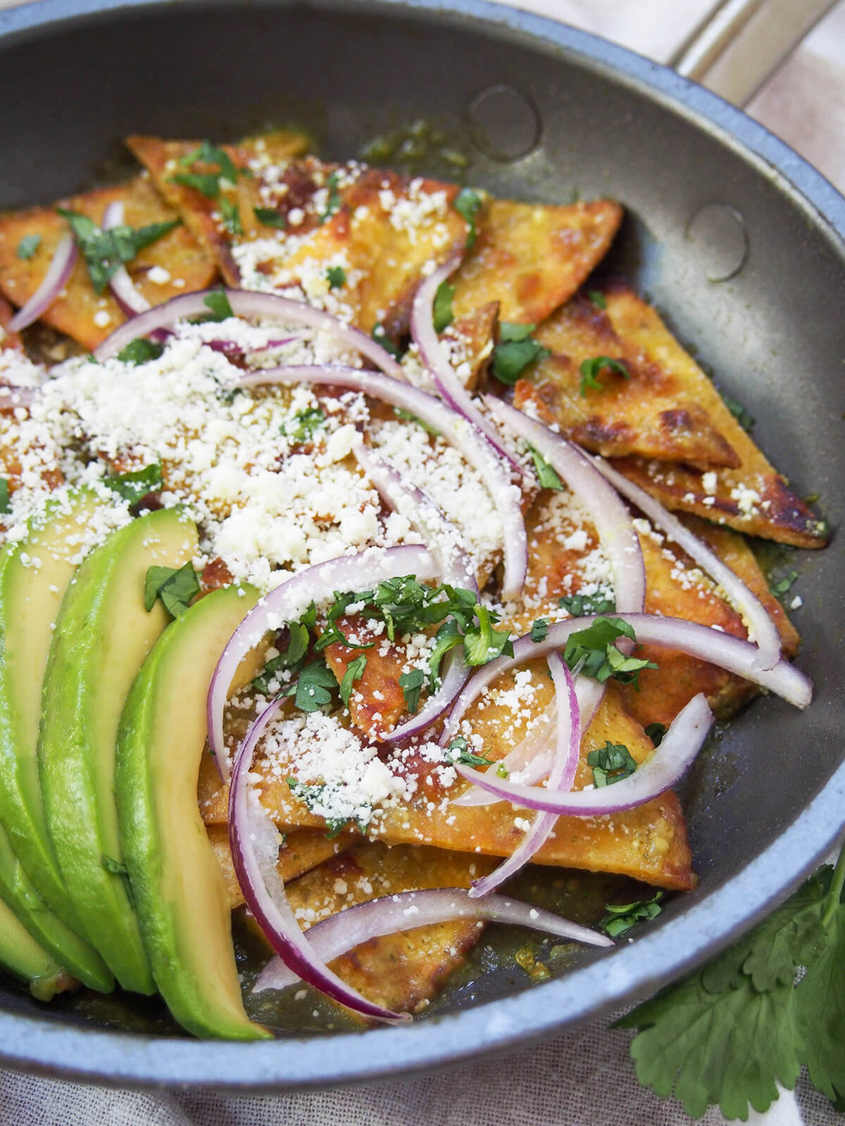 side view of chilaquiles verdes with cheese, avocado and onion on top