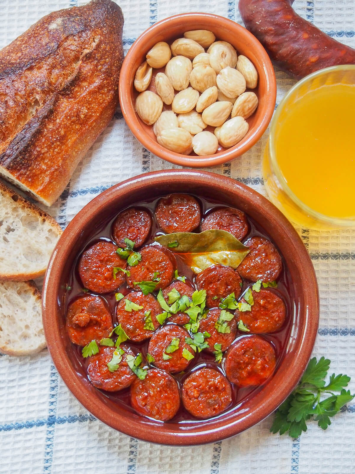 overhead view of chorizo a la sidra (chorizo in cider) with bread, dish of almonds and cider above