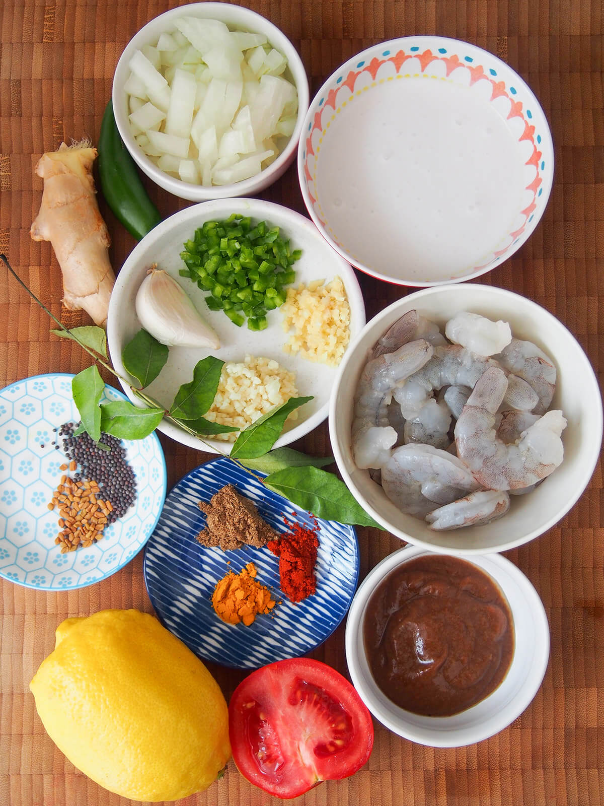 bowls of spices, onion, shrimp, coconut milk with chili and ginger to side and lemon below
