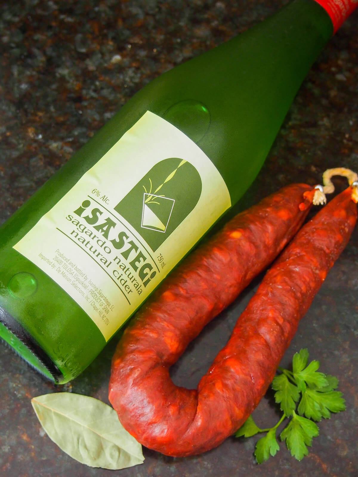 bottle of cider, whole chorizo with bay leaf and parsley below