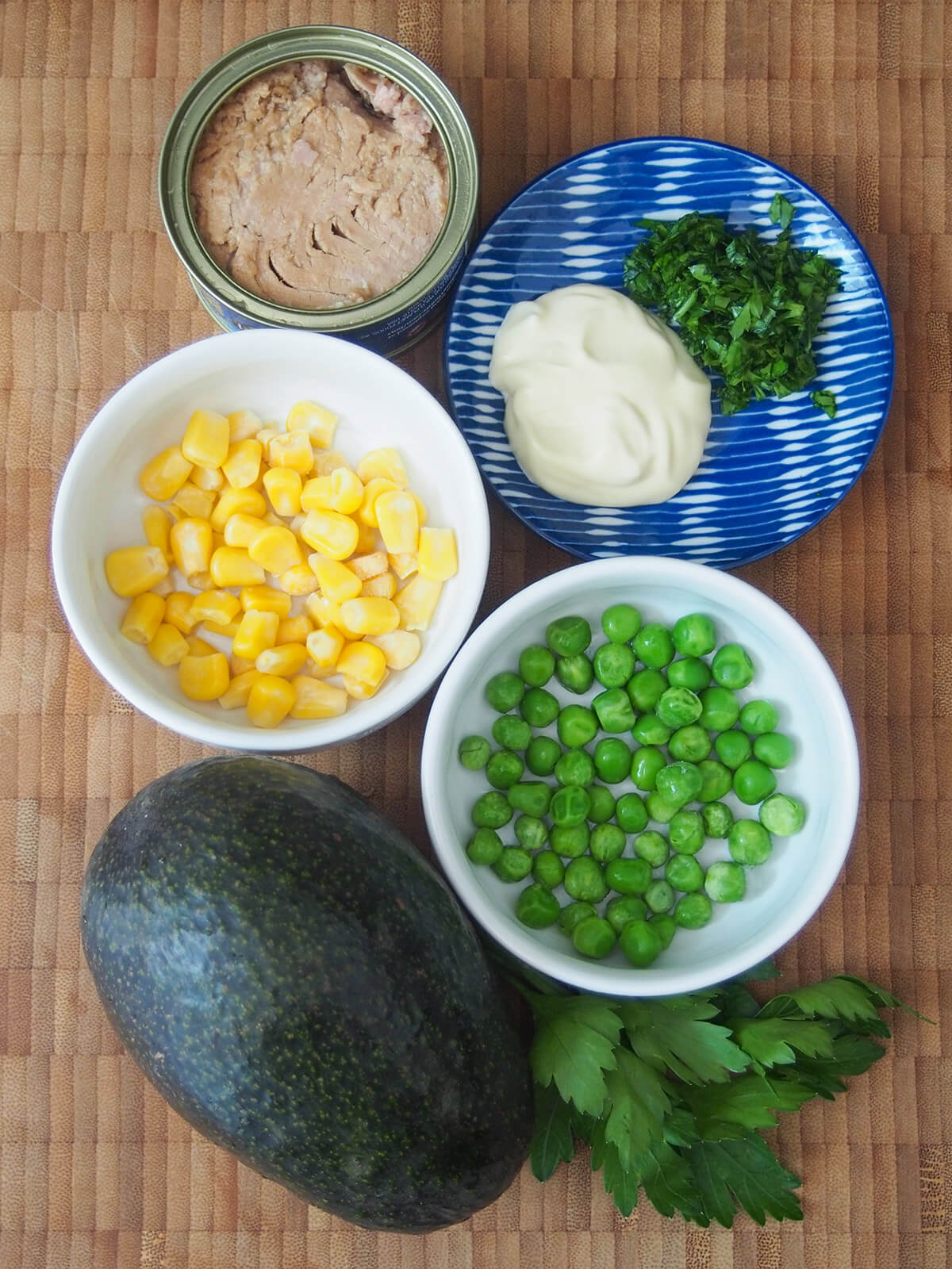 bowls of corn, peas, mayonnaise and parsley with small tin tuna and avocado to side