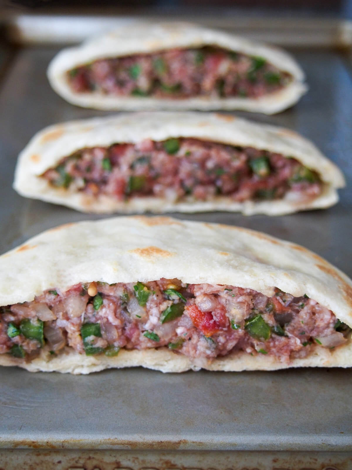 hawawshi before baking split hawawshi meat filled pita on baking sheet before cooking