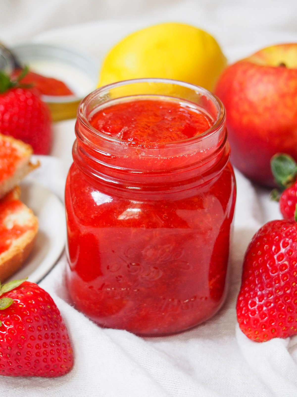jar of strawberry peach jam with lemon and peach behind and strawberries t side