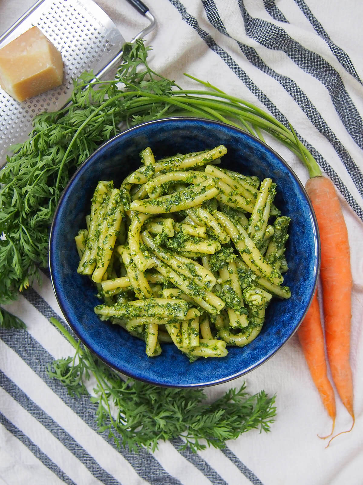 Carrot top pesto is perfect when you get carrots with greens - it has a little extra 'bite', but is just as easy and versatile as traditional pesto. Delicious with pasta, over roast carrots and more. bowl of pasta coated with carrot top pesto with carrot and block of parmesan to side of bowl