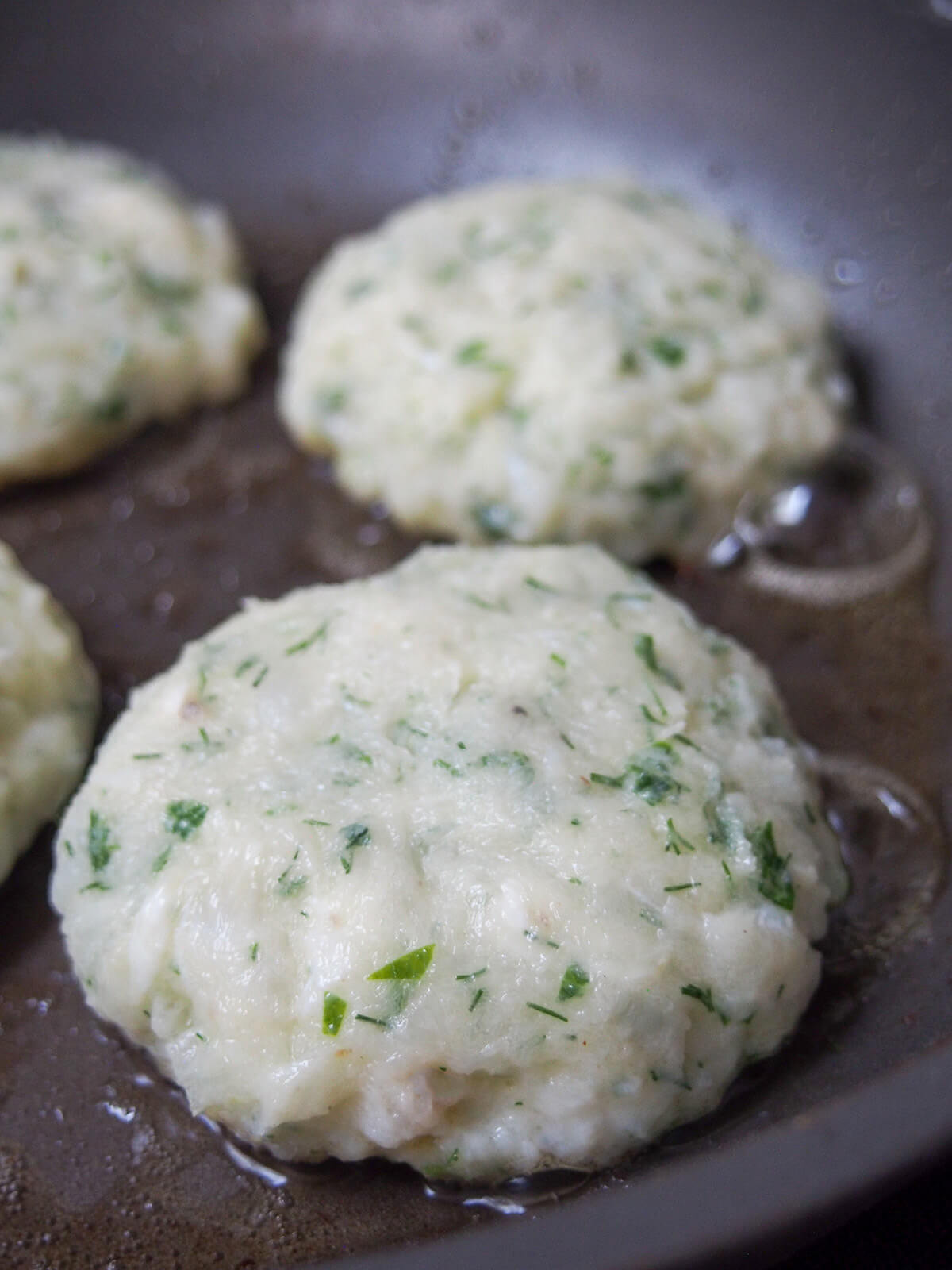 cooking fiskefrikadeller (Danish fish cakes) fish cakes cooking in skillet showing herbs in mixture