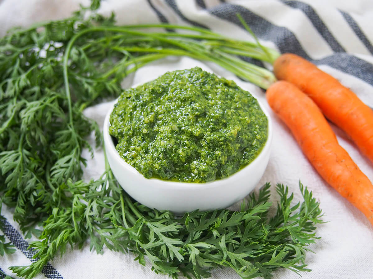 carrot top pesto bowl of carrot top pesto with carrot greens and carrots around bowl