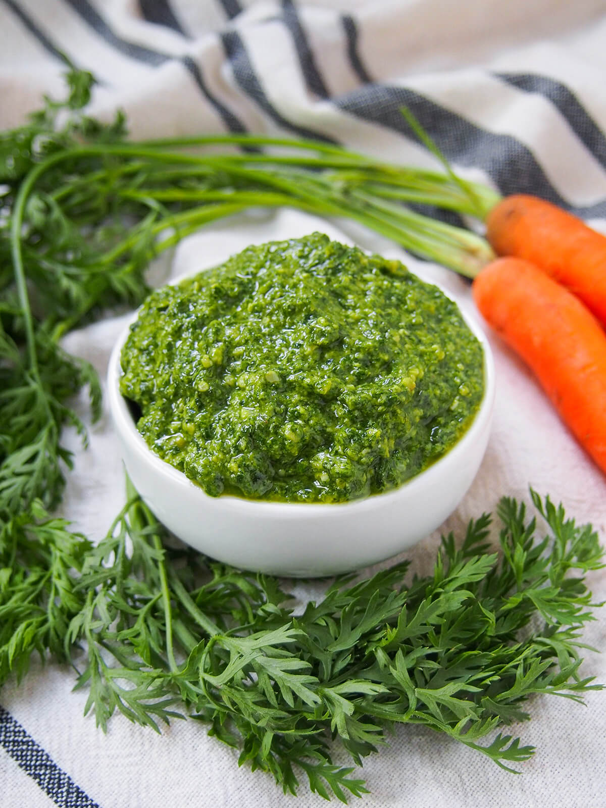 Carrot top pesto is perfect when you get carrots with greens - it has a little extra 'bite', but is just as easy and versatile as traditional pesto. Delicious with pasta, over roast carrots and more. side view of bowl of carrot top pesto with greens in front of bowl