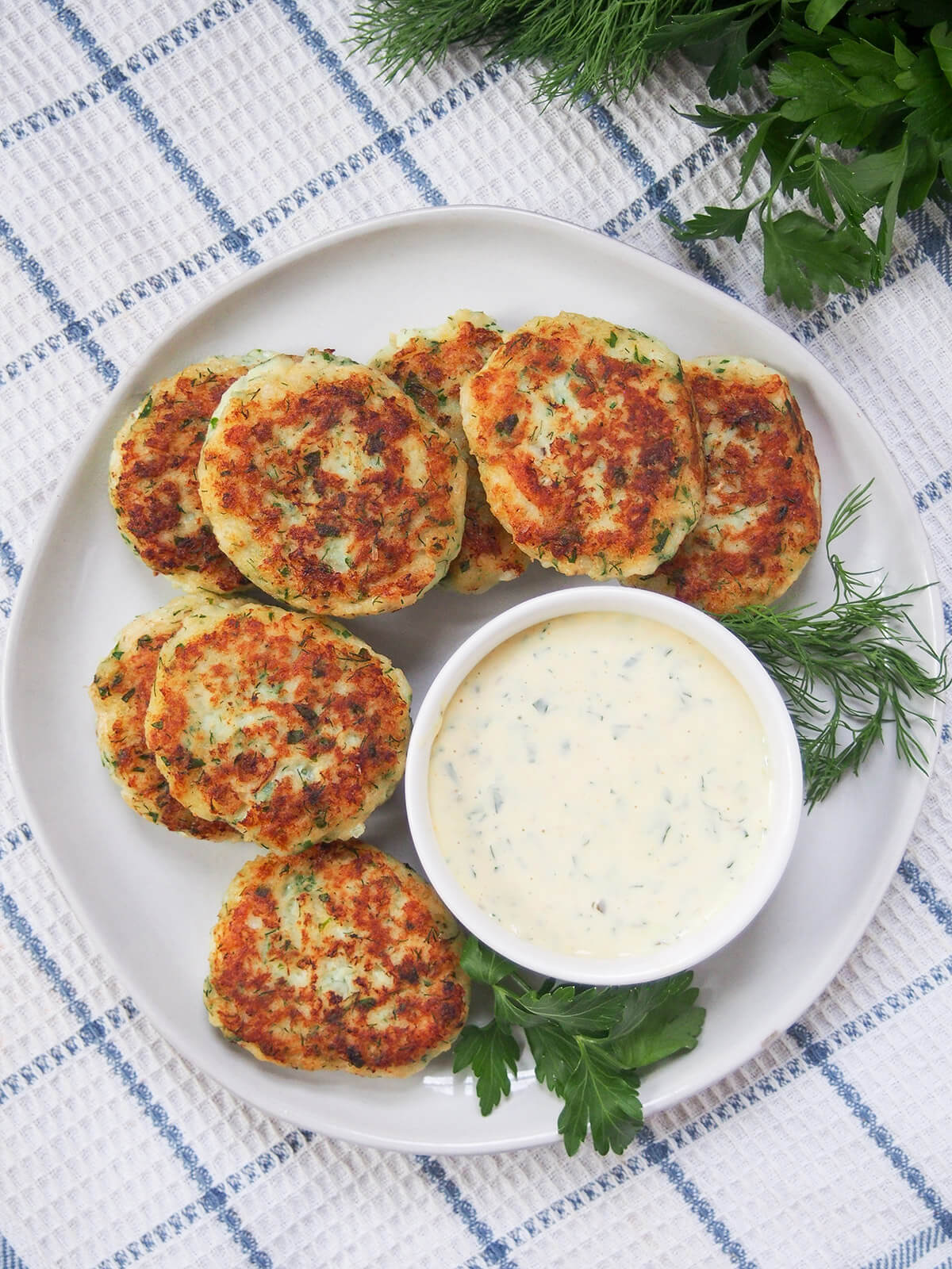 Fiskefrikadeller are simple Danish fish cakes packed with tender fish (typically cod), a touch of lemon and herbs and a splash of cream for an extra smooth texture. Easy to make, light and delicately flavored. Tasty as a main or snack, especially with some remoulade on the side. overhead view of plate of fiskefrikadeller Danish fish cakes with remoulade in small bowl on top of plate