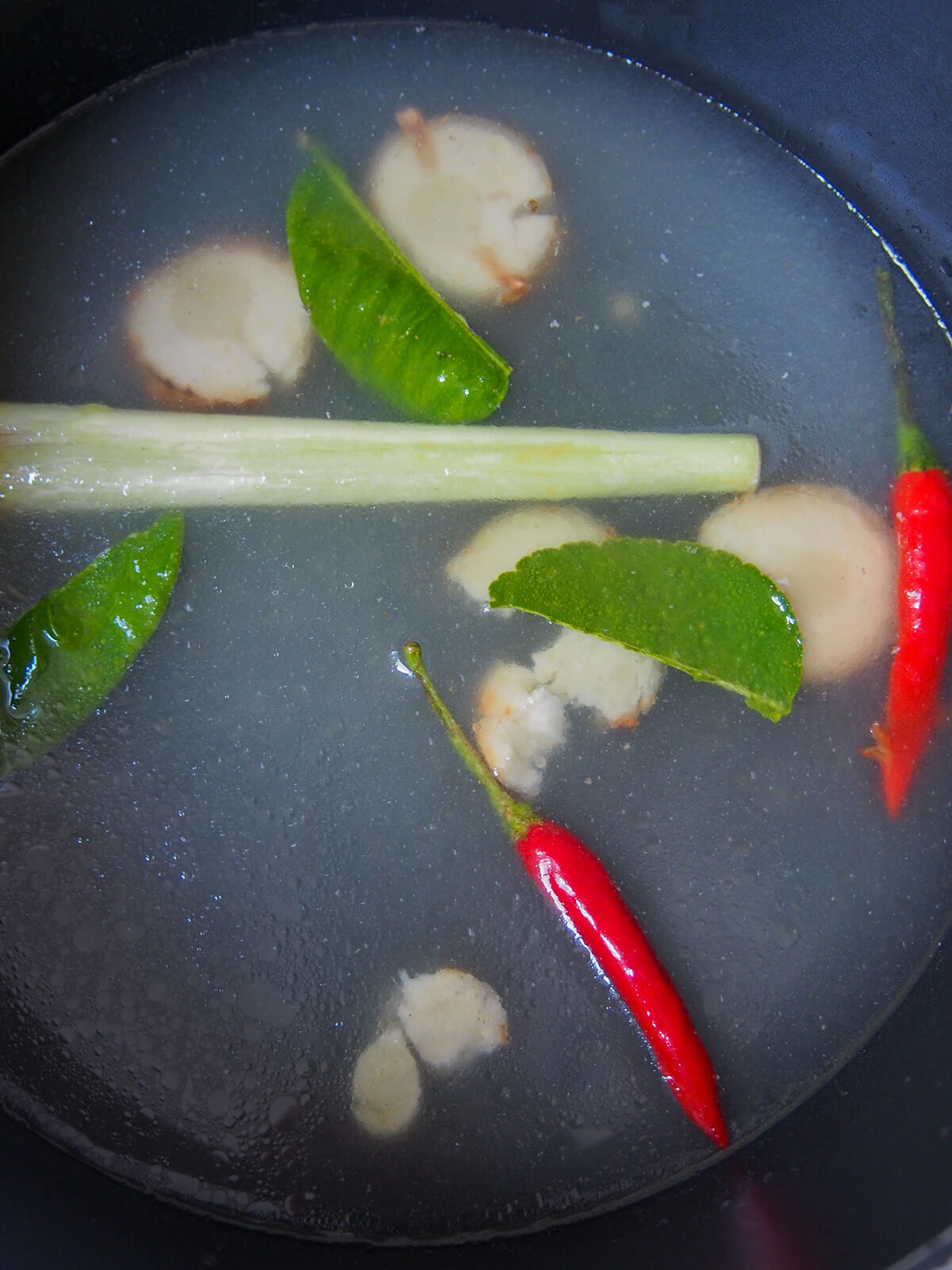 broth with lemongrass stalk, chilis, torn lime leaves and slices of galangal in it