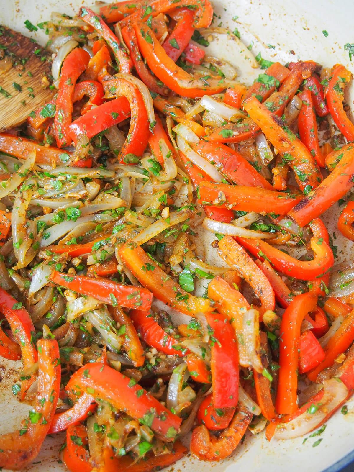 sliced peppers and onions in pan wth spices mixed through them