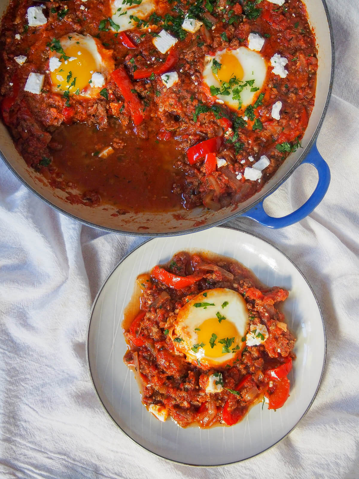small plate with portion of shakshuka with meat below dish with rest