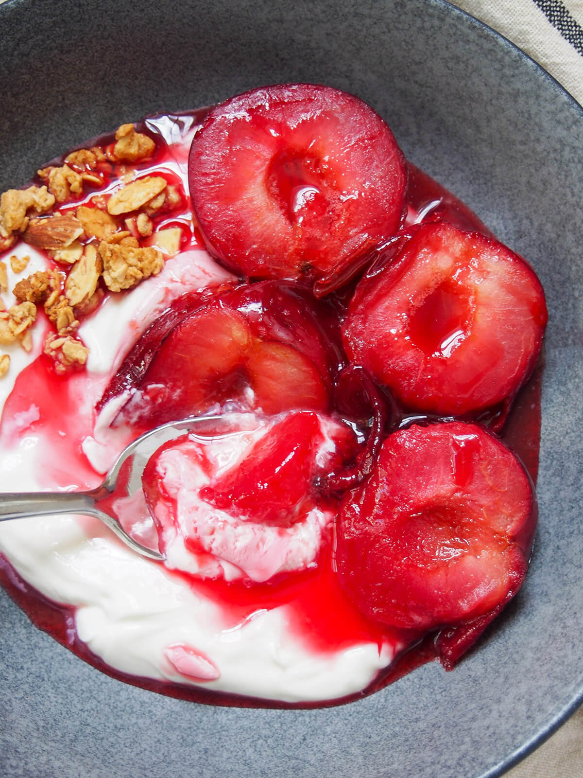 spoon in bowl taking scoop from stewed plums and yogurt