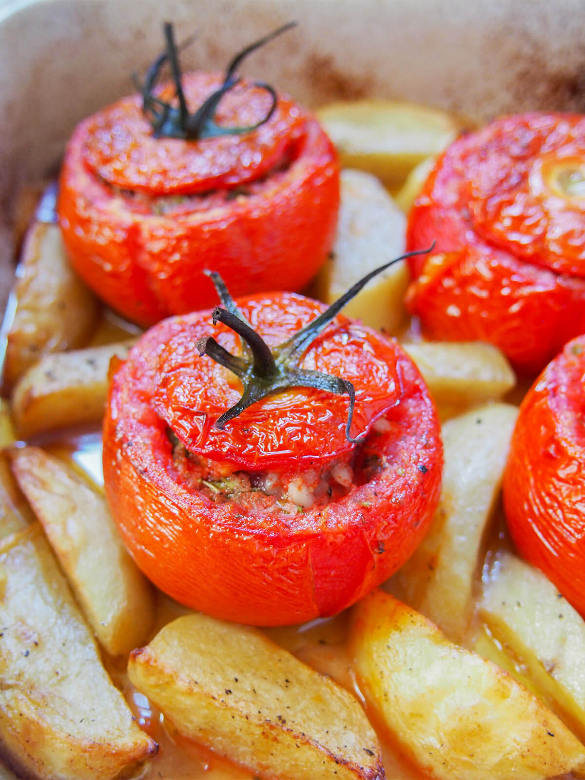 tomatoes stuffed with rice with potatoes around them in baking dish