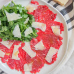 plate of beef carpaccio from overhead with arugula salad in top corner