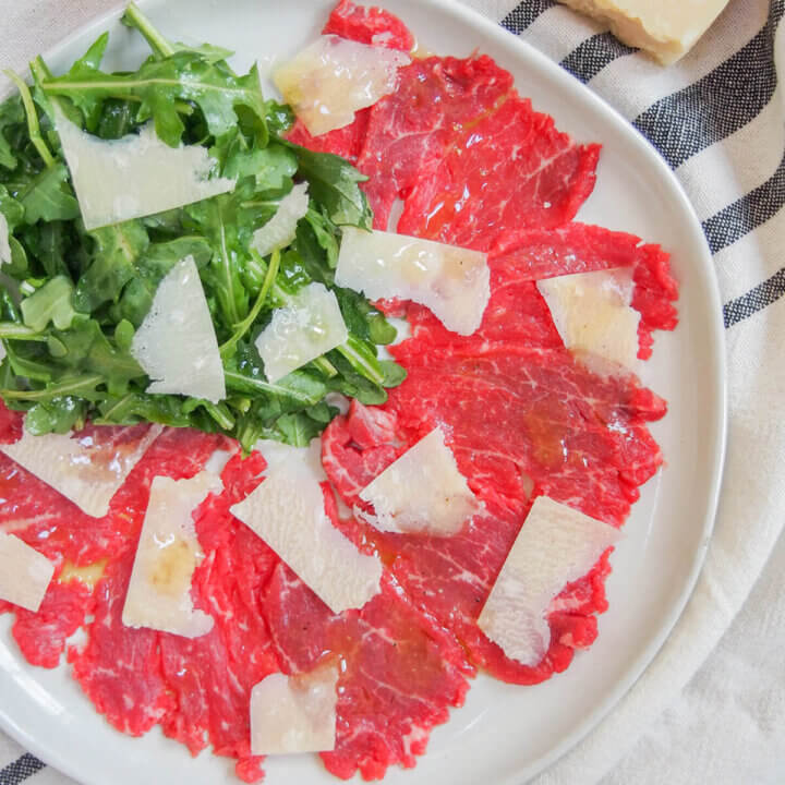 plate of beef carpaccio from overhead with arugula salad in top corner