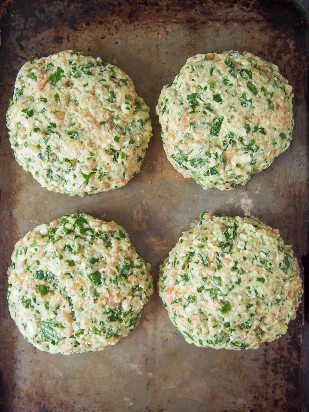 four formed spinach feta salmon burgers on baking sheet from overhead
