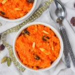 overhead view of bowl of gajar halwa carrot pudding with spoons to side