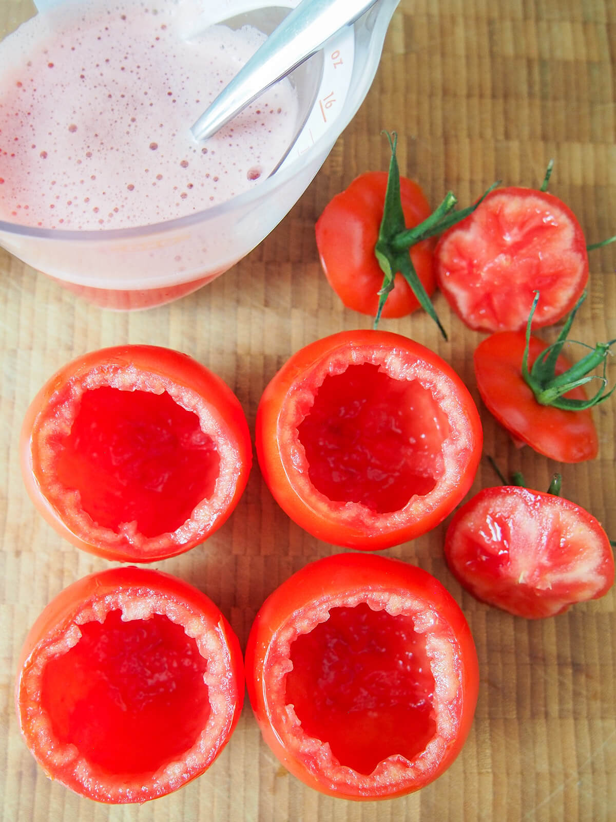 hollowed out tomatoes with tops to one side and blended pulp in measuring jug above