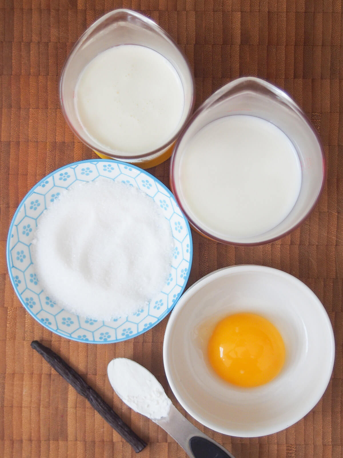measures with cream, milk, bowl of sugar and bowl with egg yolk with corn starch and vanilla pod below
