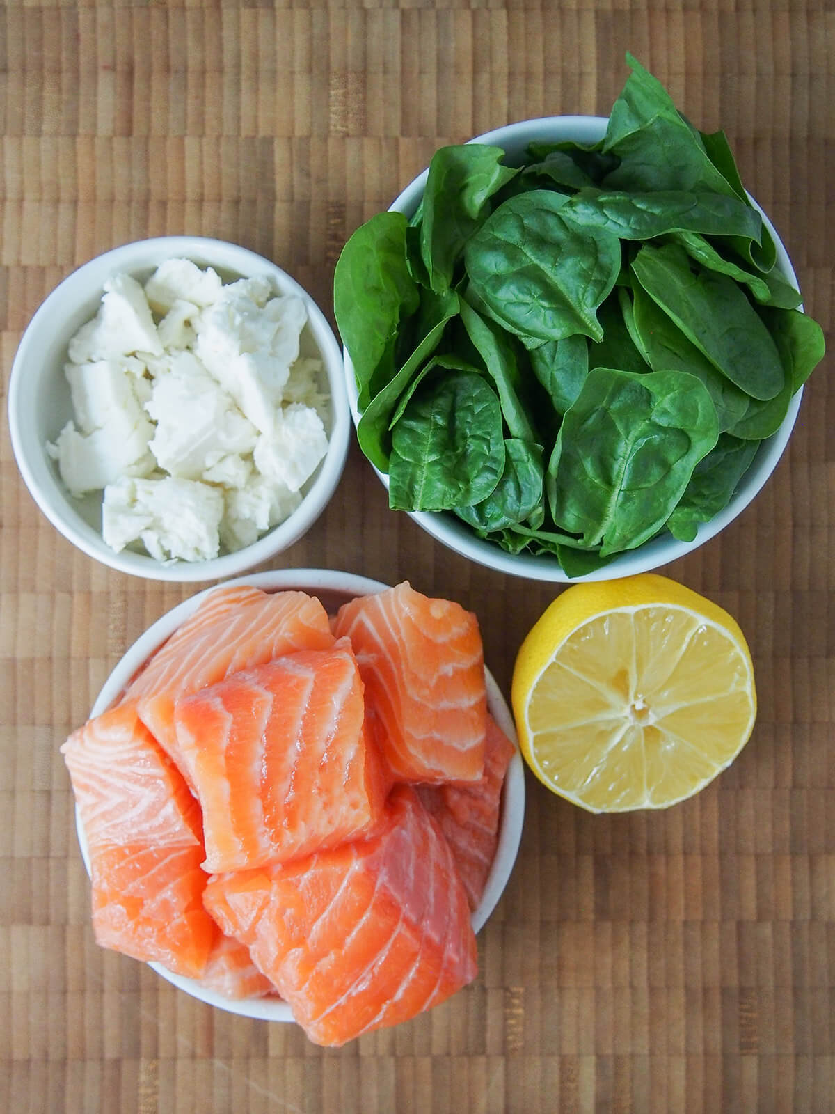 bowls with chunks of salmon, spinach leaves and crumbled feta plus half lemon to side