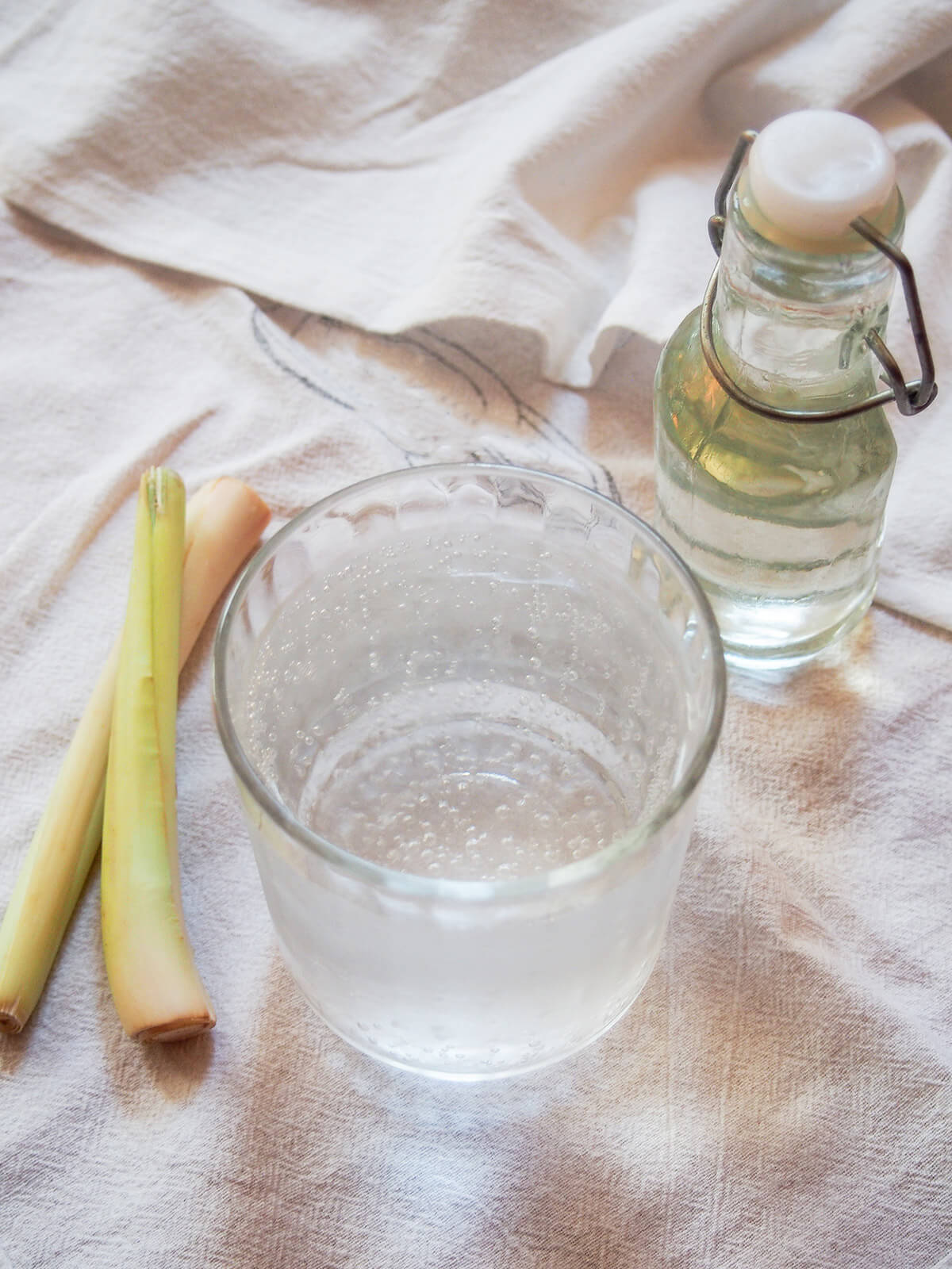 glass of lemongrass soda with bottle of syrup to one side and lemongrass stalks to other