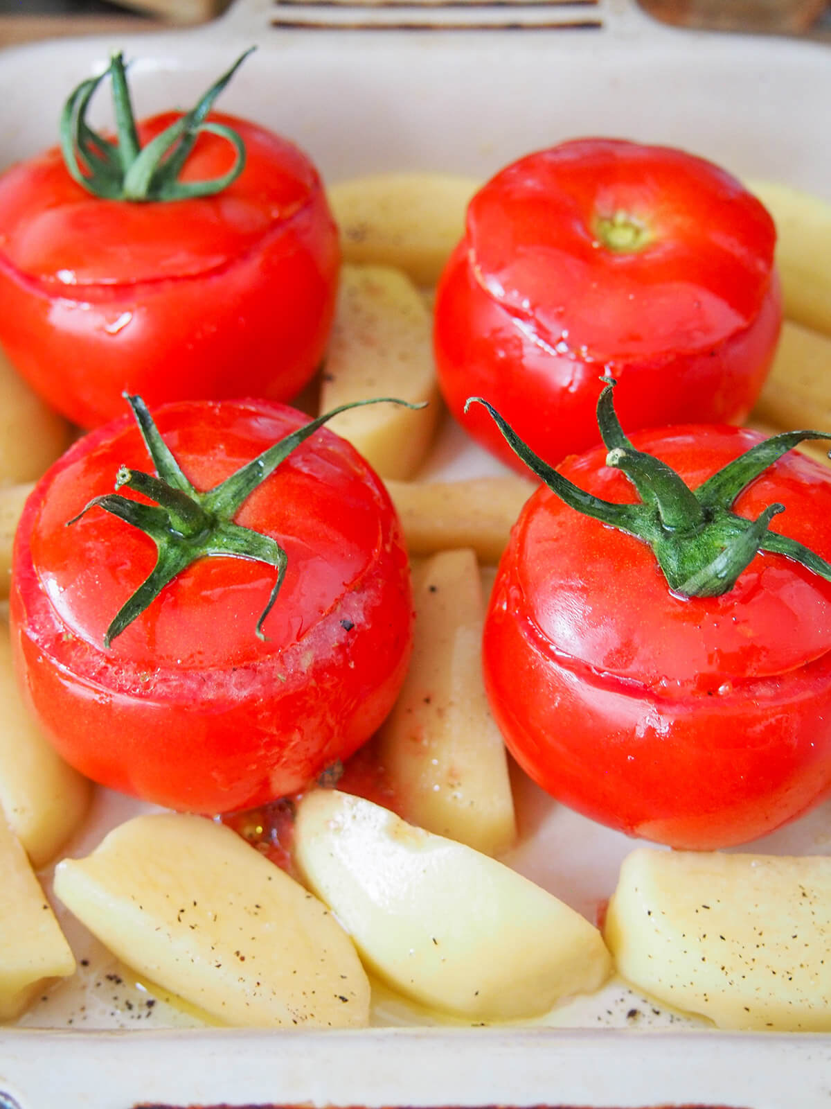 tomatoes in baking dish with potatoes around before baking