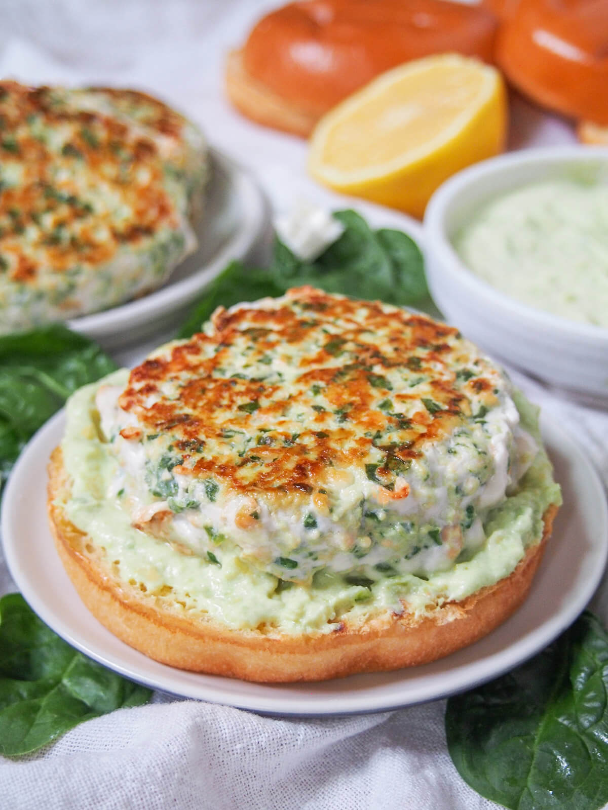 close view of spinach feta salmon burger with sauce, buns and lemon behind