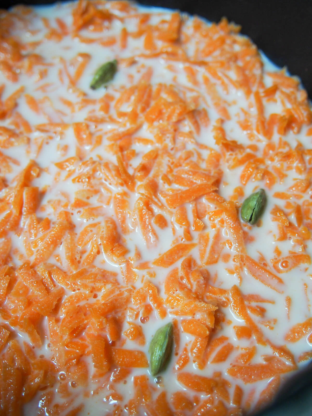 grated carrot, milk and cardamon in pot.