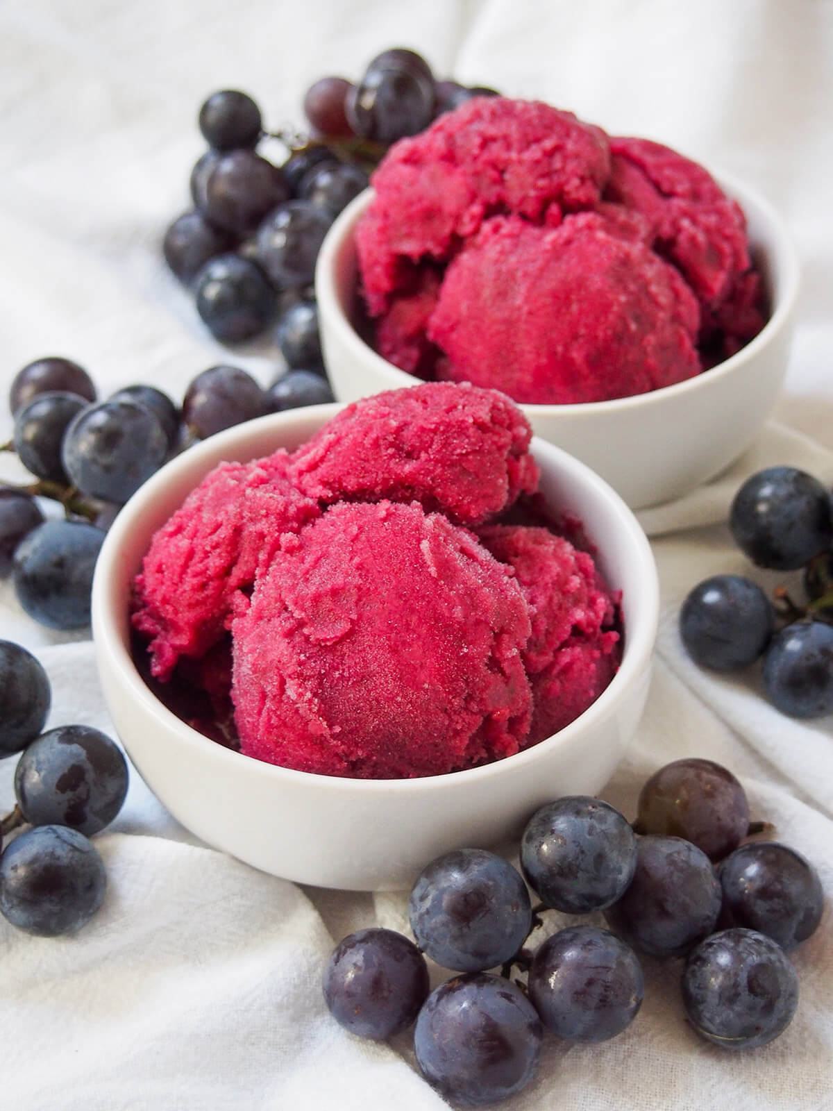 two bowls if Concord grape sorbet with grapes around bowls.