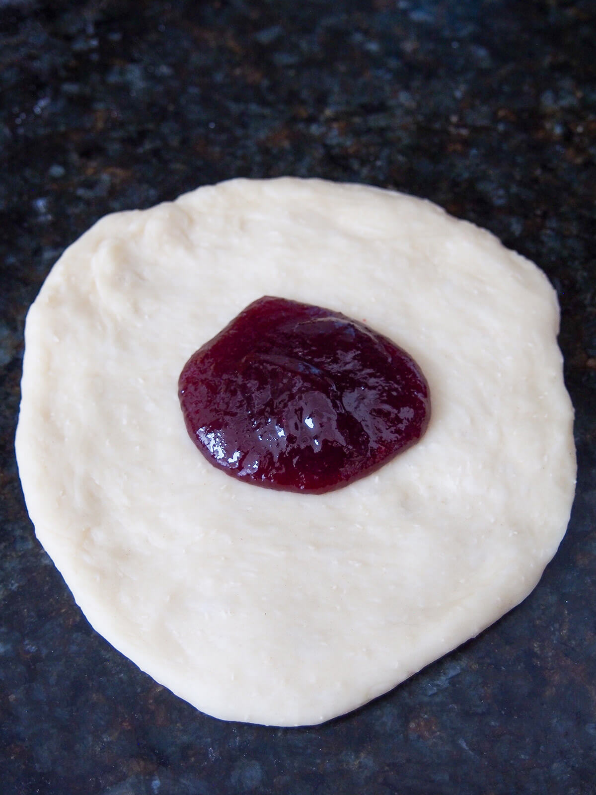 adding filling to Germknödel, traditional German/Austrian yeast dumplings plum jam on top of flattened out dough before sealing together.