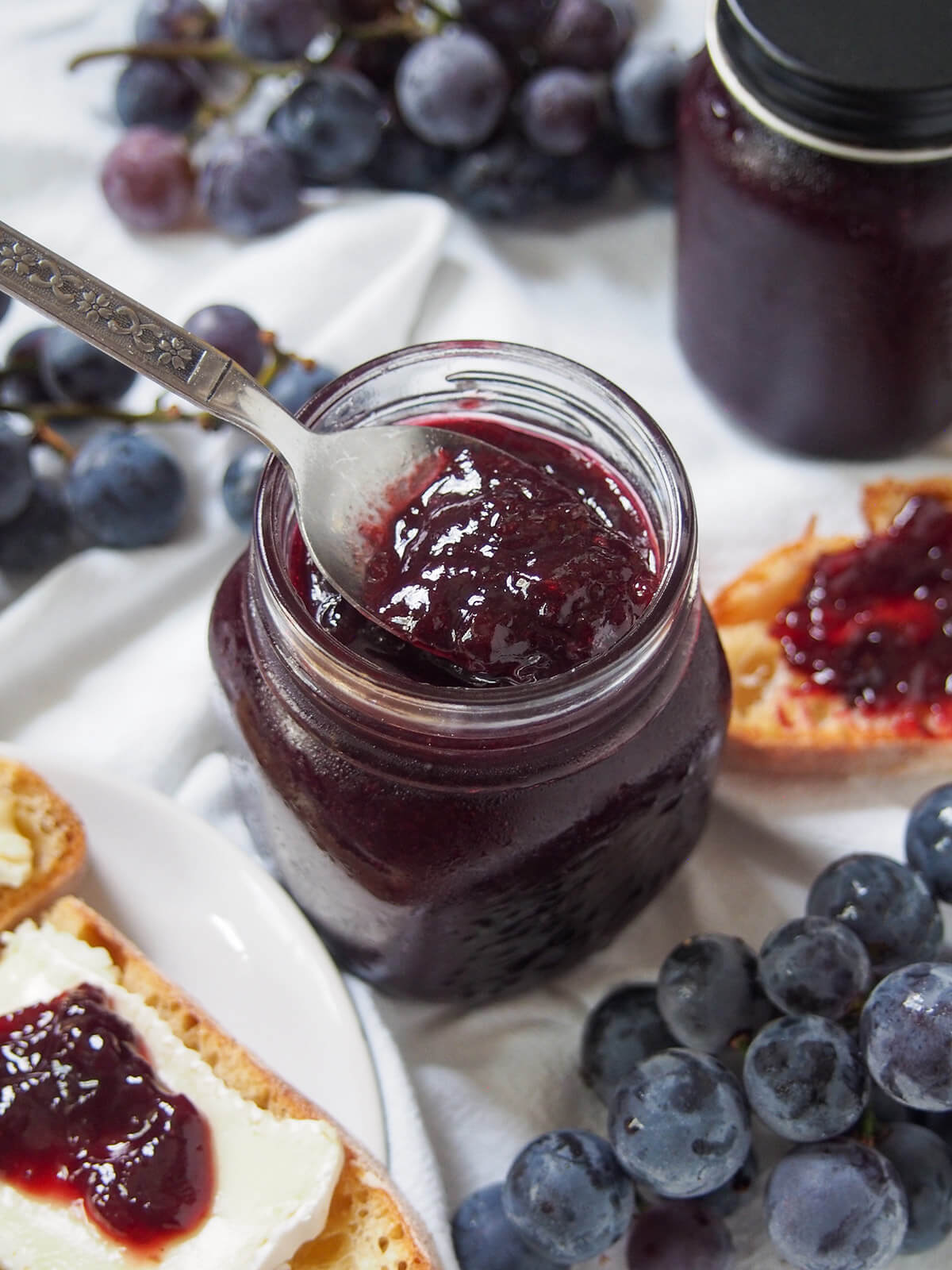 This Concord grape jam is easy to make, with no pectin, and has a wonderfully vibrant flavor and color and luscious texture. Perfect for toast, with cheese and to bake with. close overhead view of spoon in jar of Concord grape jam
