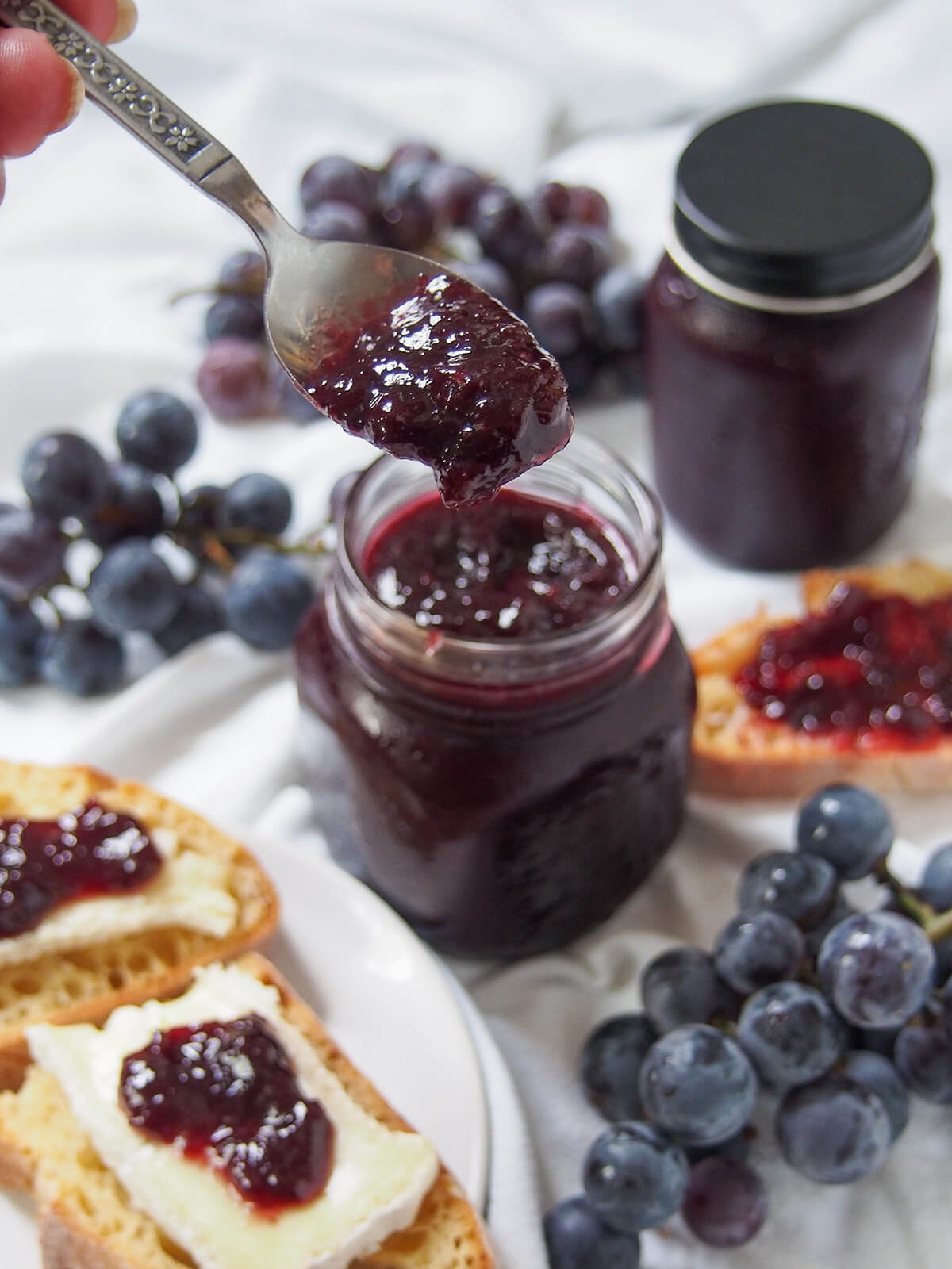 This Concord grape jam is easy to make, with no pectin, and has a wonderfully vibrant flavor and color and luscious texture. Perfect for toast, with cheese and to bake with. holding spoon of Concord grape jam over jar