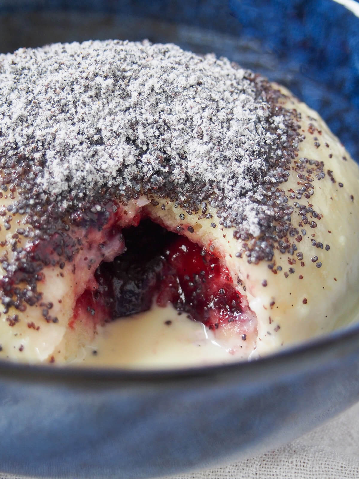 Germknödel are a traditional German/Austrian sweet yeast dumpling, filled with plum butter/jam and topped with sweetened poppy seeds. A wonderfully comforting, warming treat. close up view of Germknödel showing plum jam filling inside.