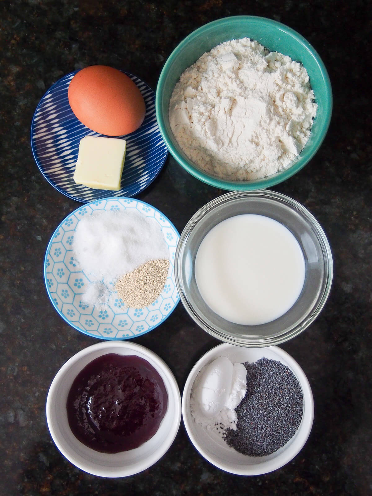 ingredients for Germknödel, traditional German/Austrian yeast dumplings bowls with flour, milk, sugar, jam, poppyseeds, egg and butter.