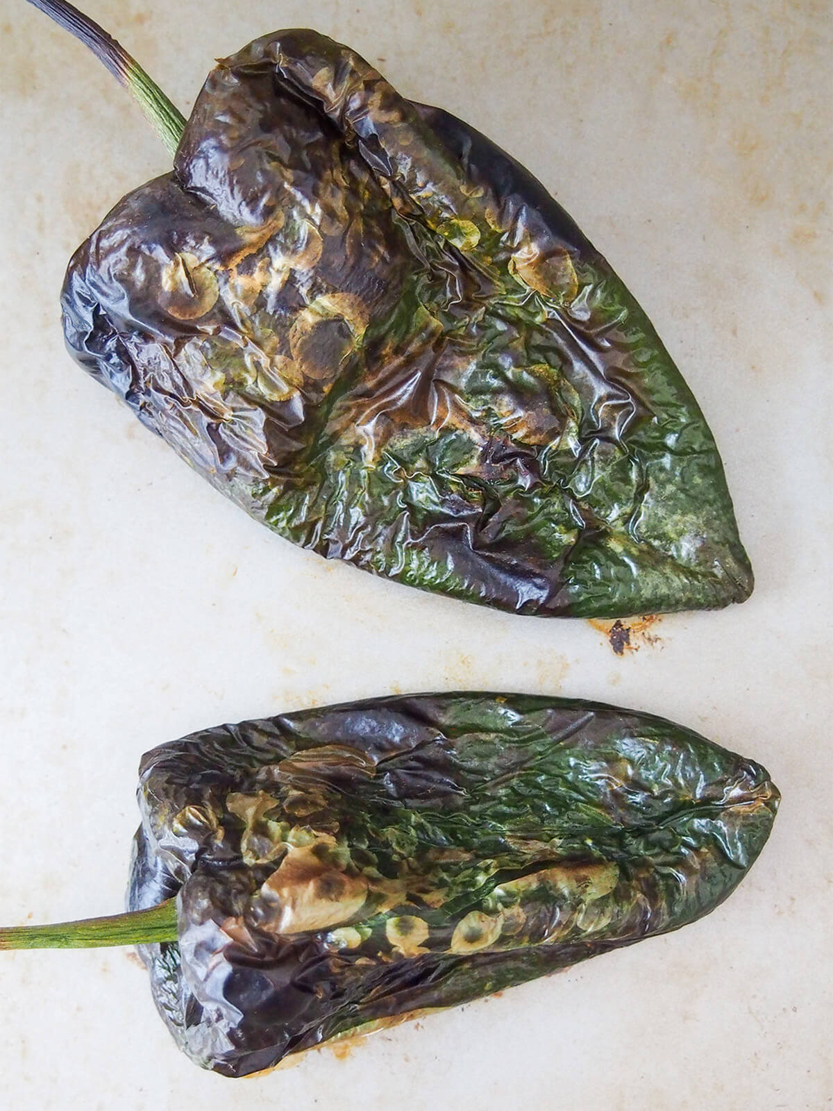 two roasted poblano peppers on baking sheet