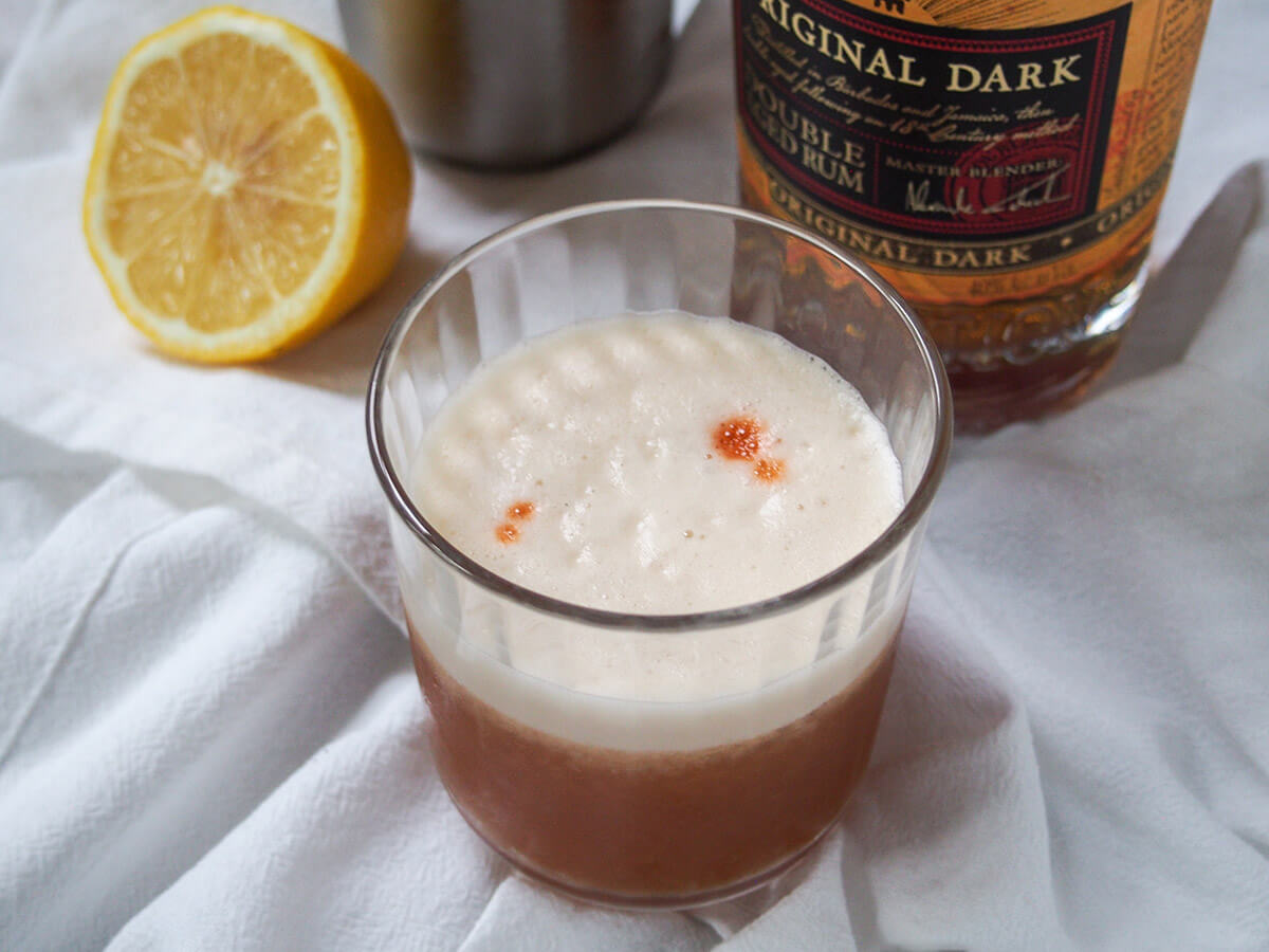 glass of rum sour with rum bottle and half lemon behind.